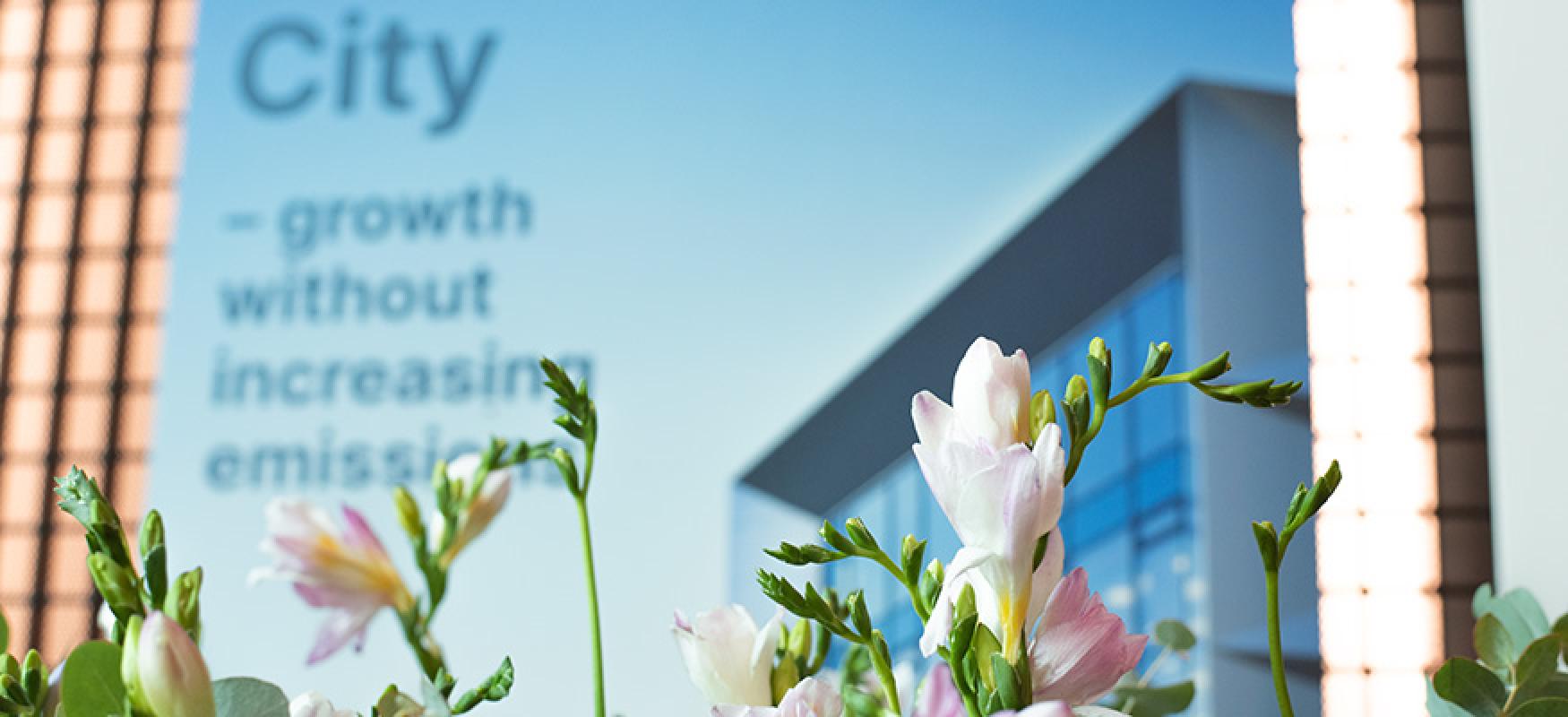 Flowers in front of a poster illustrating a house with glass window and text: growth without increasing emissions