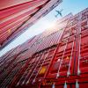 Photo of an airplane flying over stacks of red containers taken from the ground-up. 
