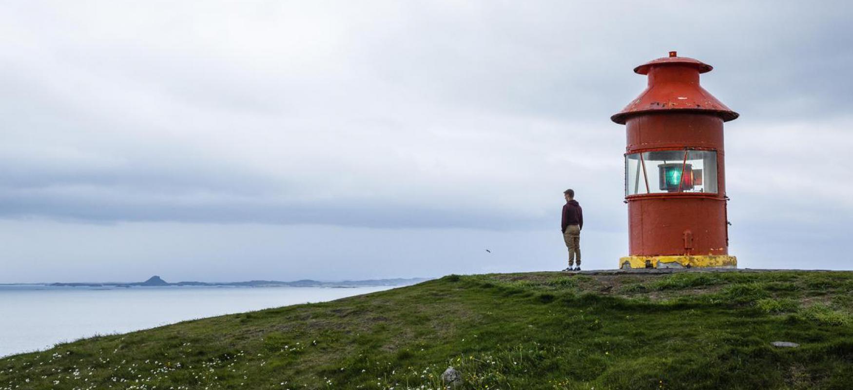 Man, standing beside lighthouse, looking at the sea in Iceland