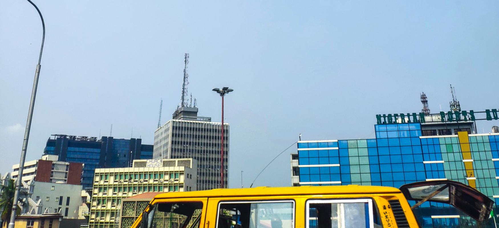 A yellow minivan driving in front of office buildings in Lagos, Nigeria.